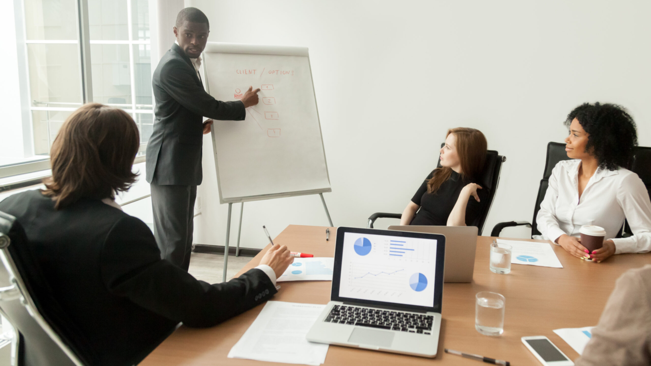 African american businessman giving presentation explains new marketing plan at meeting, black business trainer coach presenting new client management strategy at office training working on flipchart